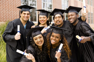 Diverse group of people dressed in cap and gowns excitedly show off diplomas after college graduation.