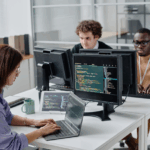 Group of young people sitting at their workplace and writing codes on computers, they working in IT office