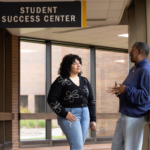 Student listening to an instructor outside of the Student Success Center on a college campus.